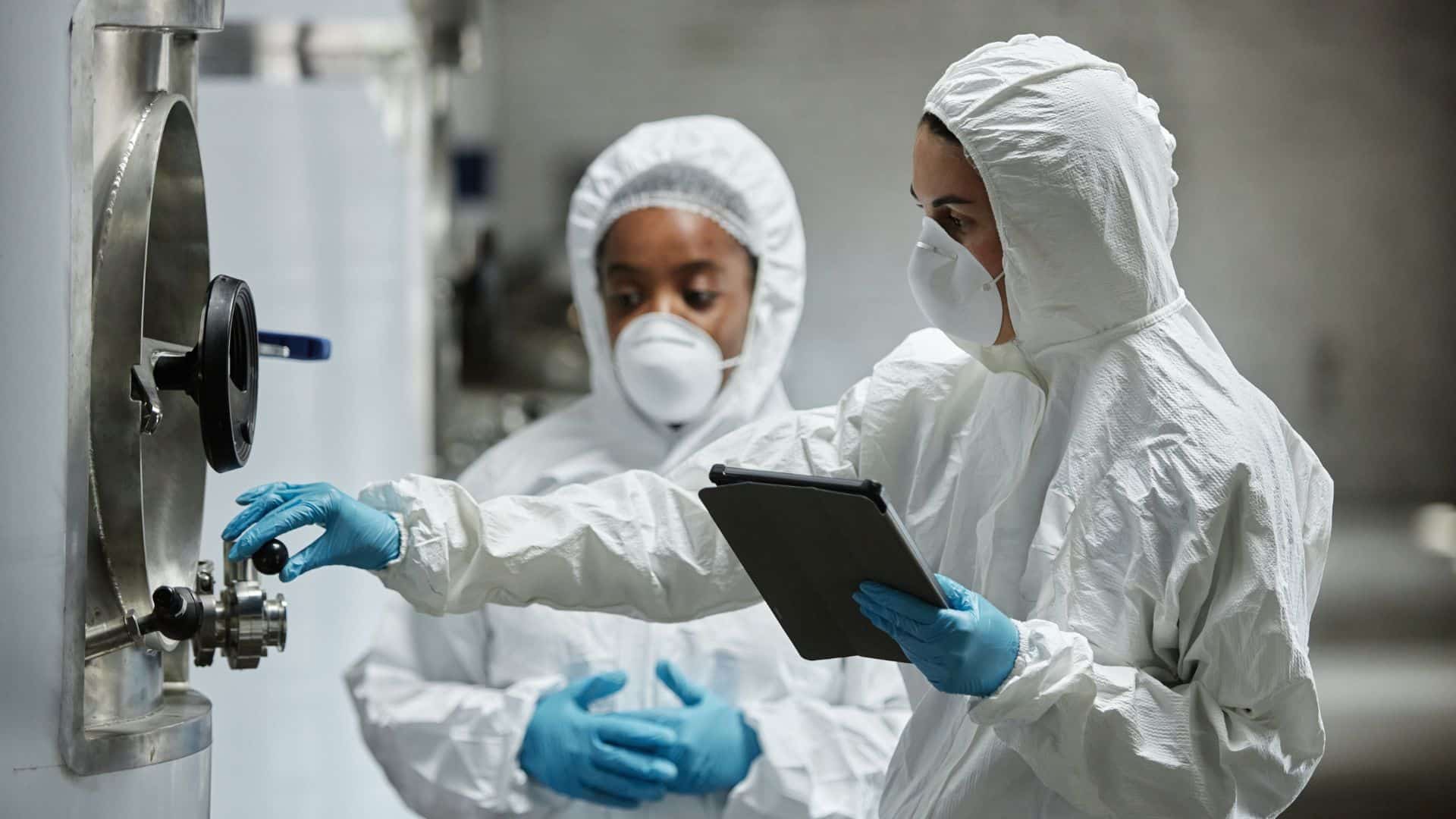 Front view of two technicians in full-body white PPE and respirators illustrating wet plant cleaning protocols.
